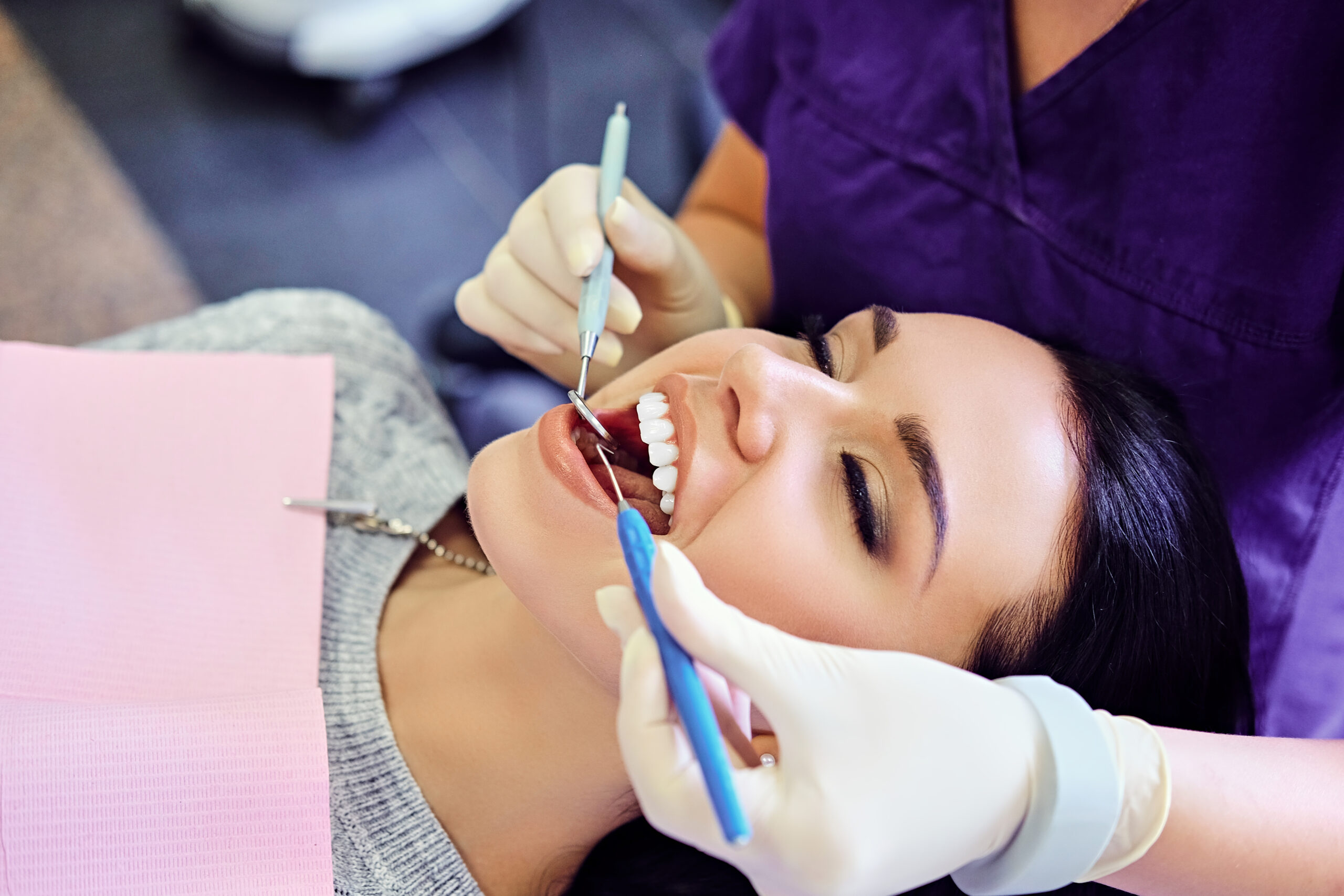 Woman smiling during a dental checkup, receiving treatment to help prevent bad breath.